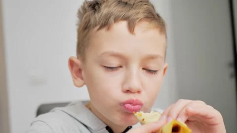 A boy eats pancakes with jam in a white kitchen. close up Video stock 228714676