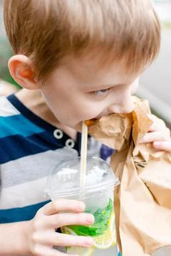The boy eats a pie and drinks lemonade on the street. Street food. Snack for  Stock Photos