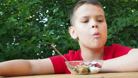 Boy eats proper nutrition and healthy breakfast bowl of oat granola with yogurt 動画素材 168019189