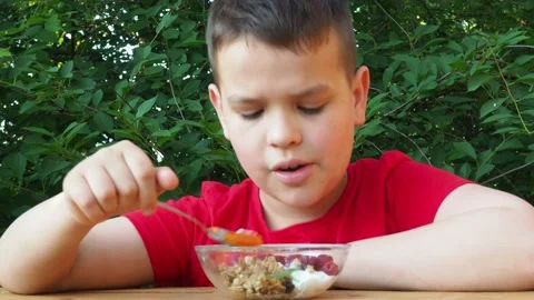Boy eats proper nutrition and healthy breakfast bowl of oat granola with yogurt 動画素材 168019192