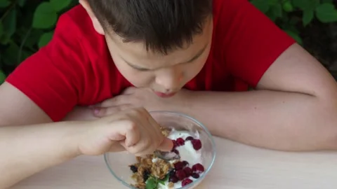 Boy eats proper nutrition and healthy breakfast bowl of oat granola with yogurt Видео 168019228