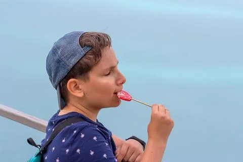 A boy eats a red lollipop outdoors. I closed my eyes from the pleasure and en Stock Photos