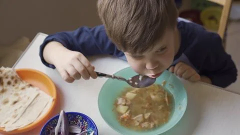 Boy eats soup sitting at dining room table with fresh onion and pita bread on it Stock Photos