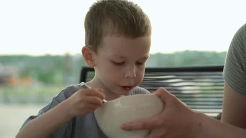 Boy eats soup with spoon from white bowl on outdoor restaurant veranda Stock-Footage 336868931