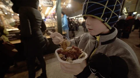 Boy eats steamy sweet snack in Salzburg market at night Stock Footage 121754884