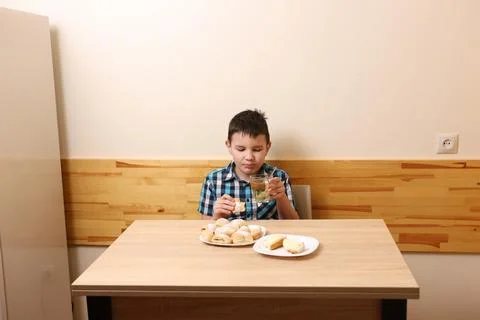 A boy eats sweet buns and drinks tea while sitting at the table. Stock Photos
