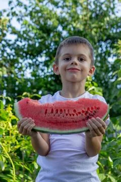The boy eats a watermelon on the background of the garden. Selective focus Stock Photos
