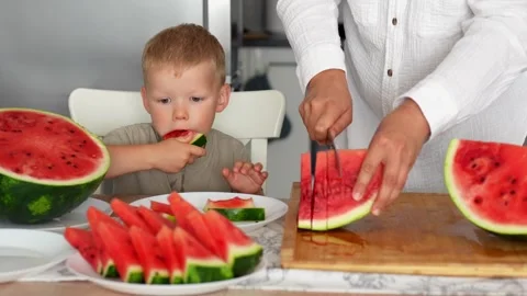 Boy eats watermelon, mom's hands cut the watermelon into triangular slices 스톡 동영상 290982059
