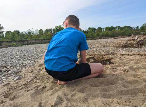 A boy on an empty wild beach playing with sand. Stock Photos