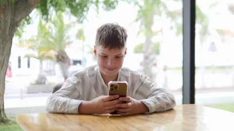Boy Engaged with Smartphone in Modern Cafe Setting Stock Footage 317004769