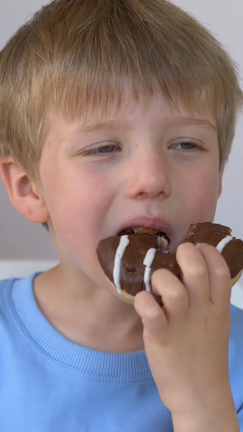 Boy enjoying chocolate donut with expressive face in closeup, food marketing Stock Footage 333680643