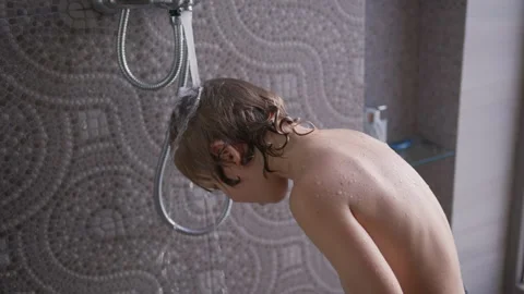 Boy enjoying a refreshing shower at home, playfully splashing water on his head Stock Footage 296715121