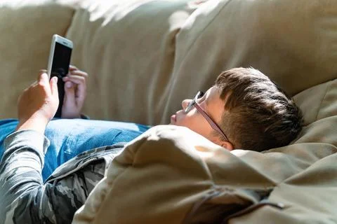 Boy enjoys his smartphone while lounging on a comfortable couch Stock Photos