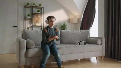 Boy Enjoys Music on Sofa. Relaxed child headphones digital leisure cozy home Stock Footage 335482964