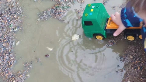 The boy is exploring the muddy puddle with his hand, feeling the texture of the Stock Footage 251630628