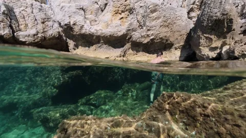 Boy exploring sea cave split shot over under half underwater view 스톡 동영상 338181725