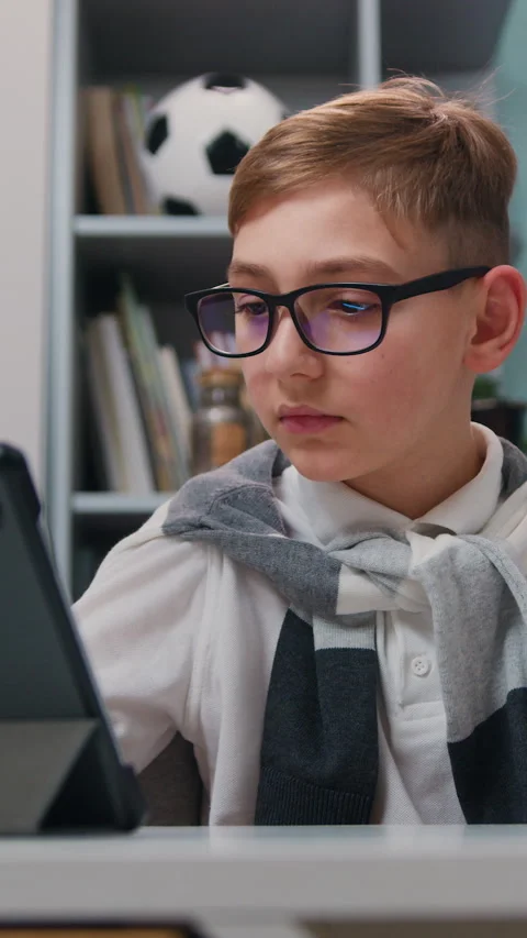 Boy in eyeglasses using tablet computer for online education at home. Distance e Stock Footage 329889493
