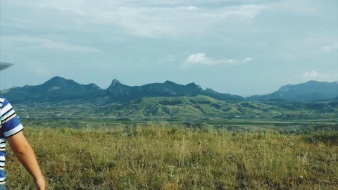 The boy in a felt hat walks the hill and looks at the mountains Stock Footage 79388017