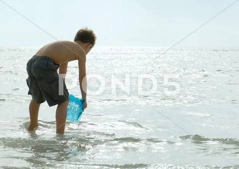 Boy Filling Bucket With Water In Surf