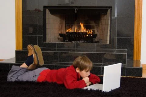 Boy at fireplace on computer. Stock Photos