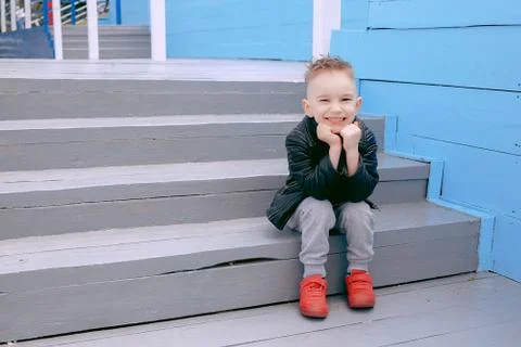 A boy of five, sits on the steps, smiles happy at life, poses on the camera Stock Photos