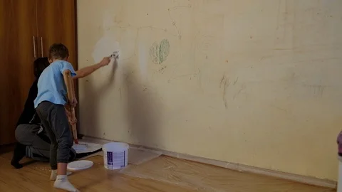 A boy of five years paints a wall with drawings of white paint. Next to him is Stock Footage 118886893