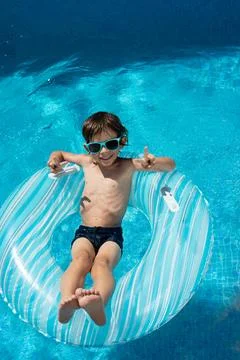 Boy on float wearing sunglasses and swimsuit in pool Stock Photos