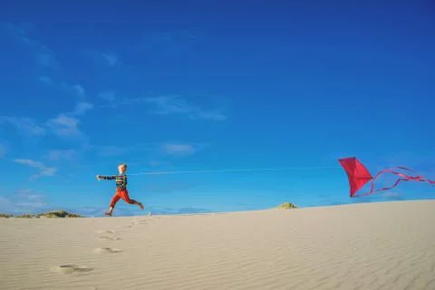 Boy flying red kite on sandy beach Stock Photos