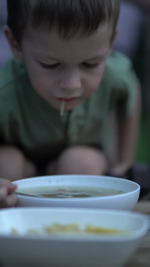 Boy with focused expression eats soup from white bowl using metal spoon  Video stock 343138758