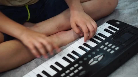 Boy fooling around playing black electronic piano synthesizer sitting on bed in  Stock Footage 307490461