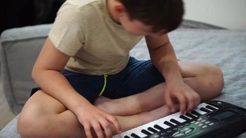 Boy fooling around playing black electronic piano synthesizer sitting on bed in  Stock Footage 307490468