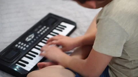 Boy fooling around playing black electronic piano synthesizer sitting on bed in  Stock-Footage 307490509