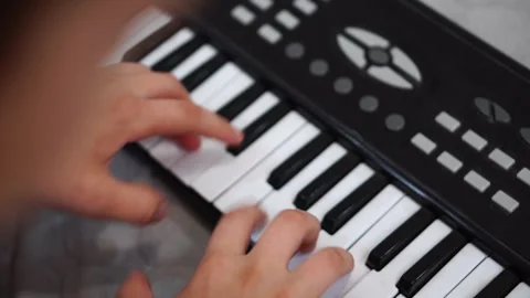 Boy fooling around playing black electronic piano synthesizer sitting on bed in  Stock Footage 307490537