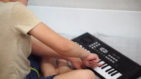 Boy fooling around playing black electronic piano synthesizer sitting on bed in  Video stock 307490620