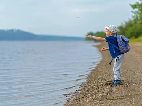 A boy of four years by the river throws stones into the water. Stock Photos