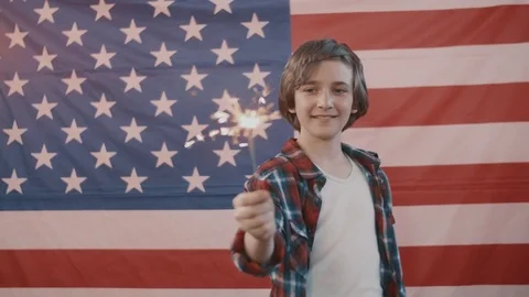 Boy in front of american flag holding sparkler in hand. shot in slow motion Stock Footage 75779927