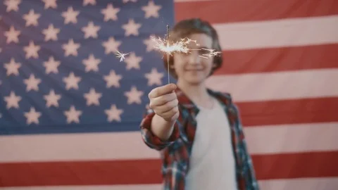 Boy in front of american flag holding sparkler in hand. shot in slow motion Stock Footage 75780126