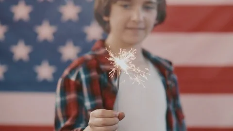Boy in front of american flag holding sparkler in hand. shot in slow motion Stock Footage 75780456