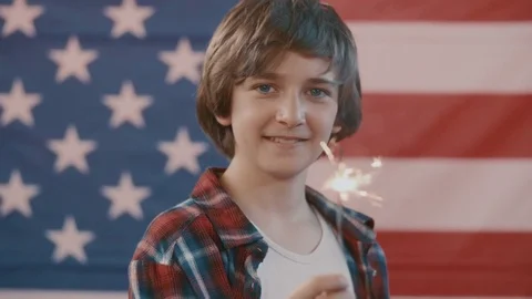 Boy in front of american flag holding sparkler in hand. shot in slow motion Stock Footage 75780574