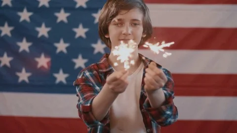 Boy in front of american flag holding sparklers in hands. shot in slow motion Stock Footage 75784720