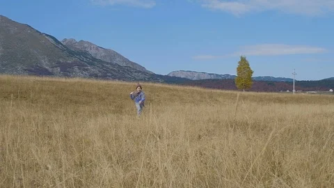 Boy in a funny hat runs through the autumn field on the background of mountains. Vídeo Stock 98365042
