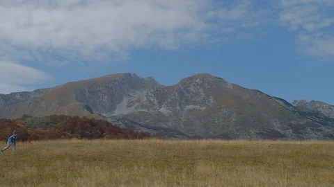 Boy in a funny hat runs through the autumn field on the background of mountains. Stock Footage 98366304