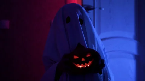 Boy in ghost costume for Halloween with pumpkin in his hands. Scary ghost stands Stock Footage