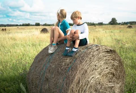 Boy with a girl sitting on  haystack  the background of summer meadows Stock Photos