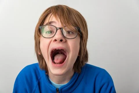 Boy with glasses and blue jacket yelling toward the camera, mouth wide open.. Stock Photos