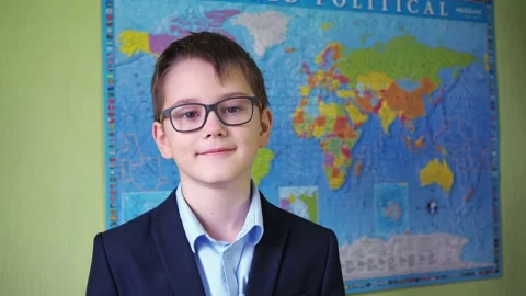 A boy in glasses and a jacket stands against the background of a world map. a Stock Footage 166233981