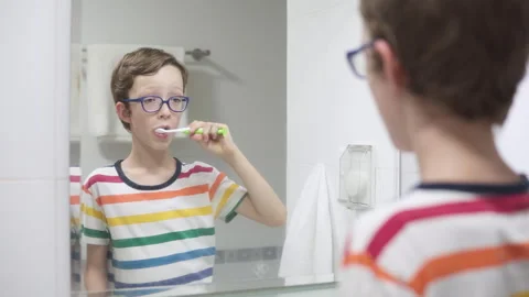 Boy in glasses is brushing his teeth at a bathroom Stock Footage 345381379
