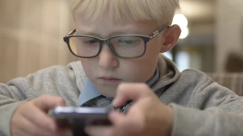 The boy with glasses carefully looks at the screen of a mobile phone Stock Footage 116498449