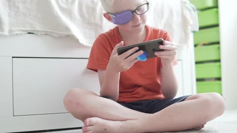 A boy with glasses with a glued eye uses a mobile phone at home Stock Footage 133091673