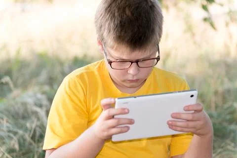 The boy in glasses looks tablet computer at nature Stock Photos